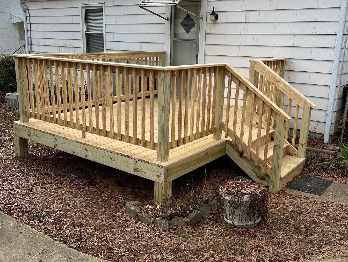A wooden deck with stairs is in front of a white house.