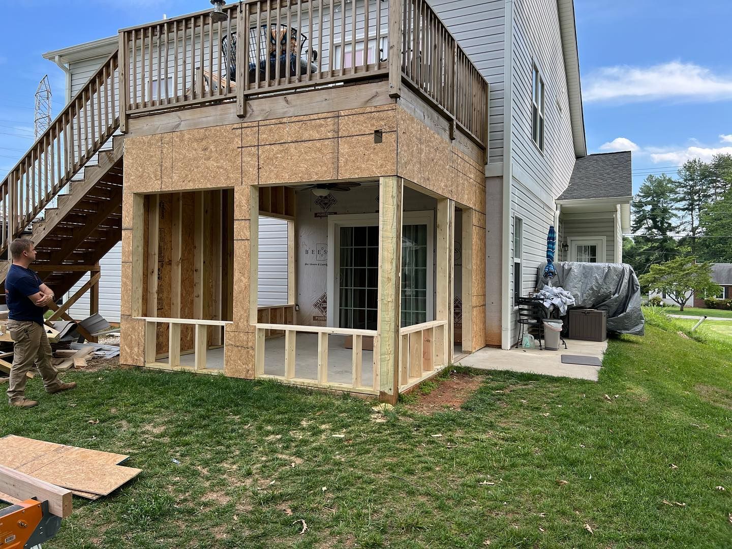 A man is standing in front of a house with a screened in porch under construction.