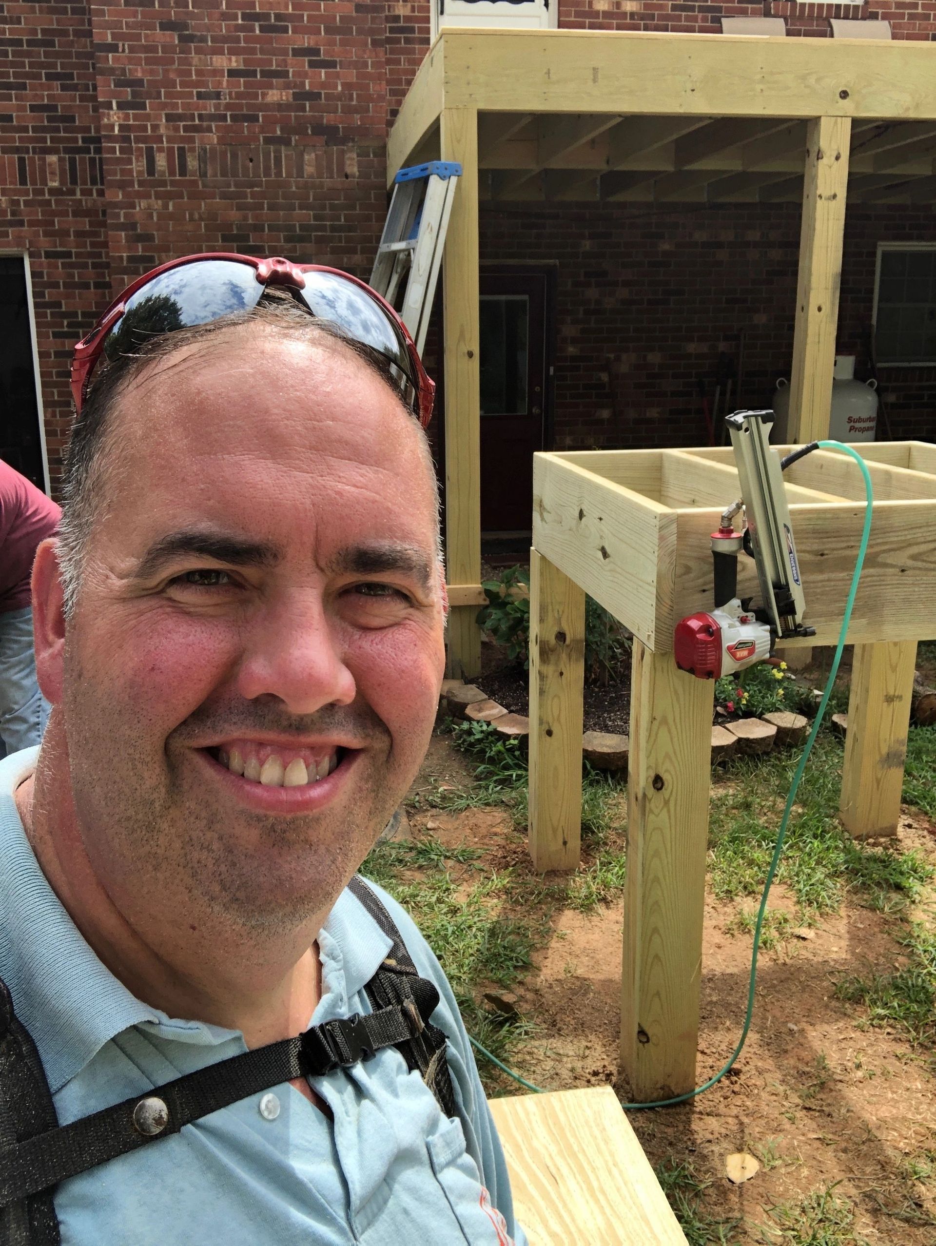 A man is smiling while standing in front of a wooden structure.