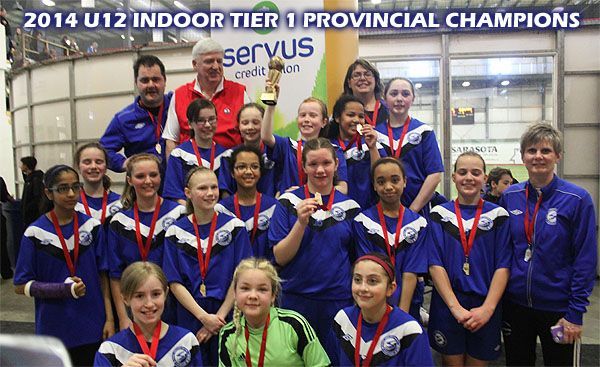 A soccer team poses with a trophy and gold medals in an indoor arena under a sign reading 2014 U12 Provincial Champions.
