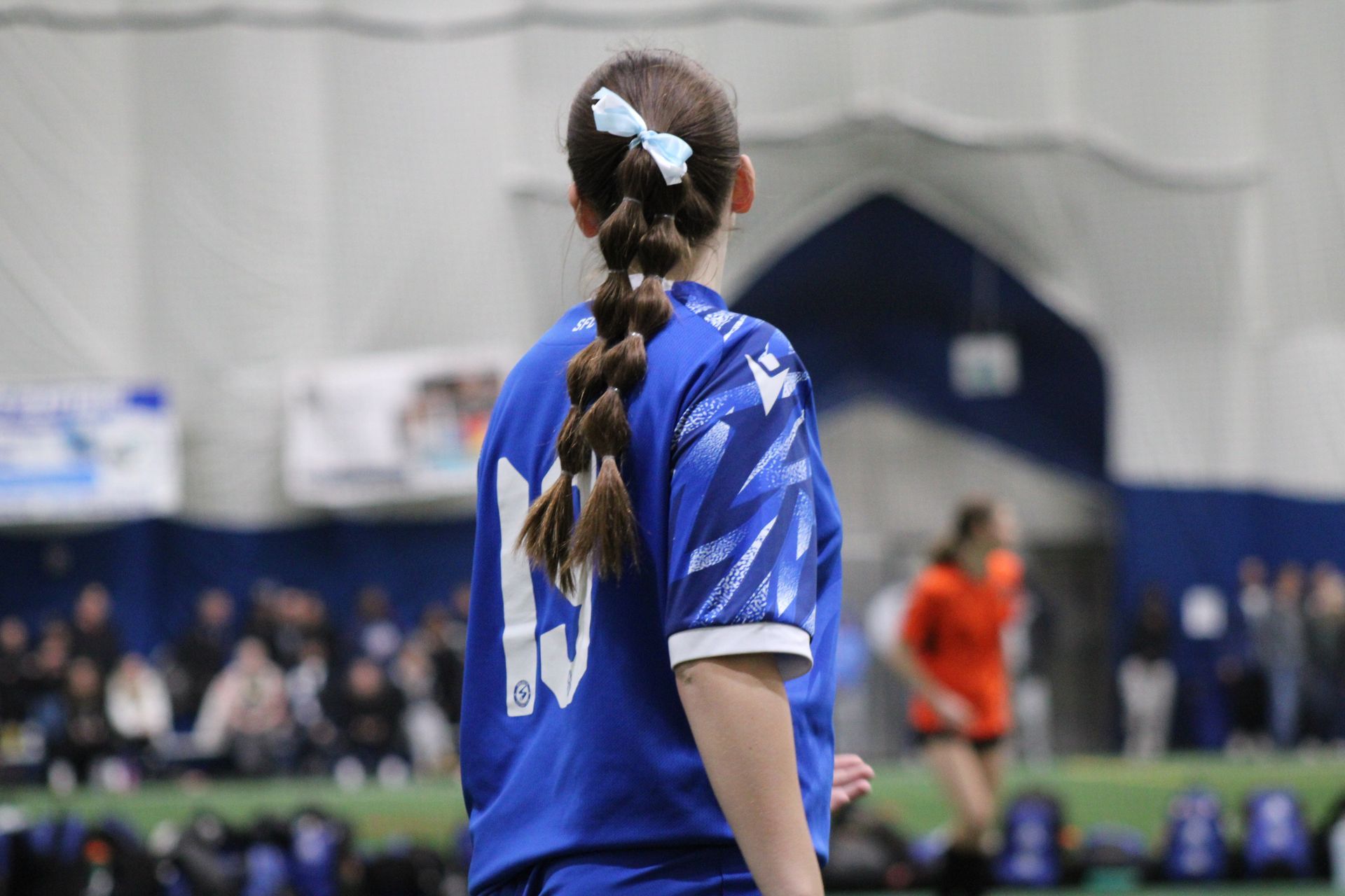 A player wearing a blue jersey with the number 19 stands on an indoor field, viewed from behind.