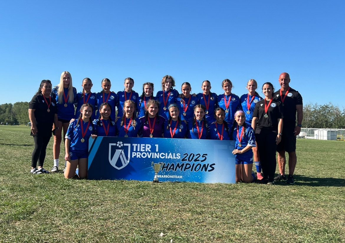 A sports team in blue jerseys stands on a field holding a banner that says 