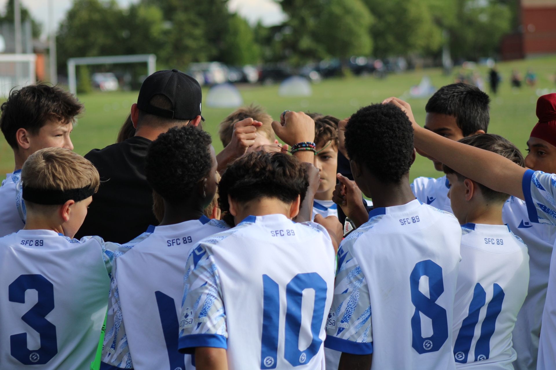 A soccer team in white and blue jerseys huddles together on a field with their hands joined in the center.