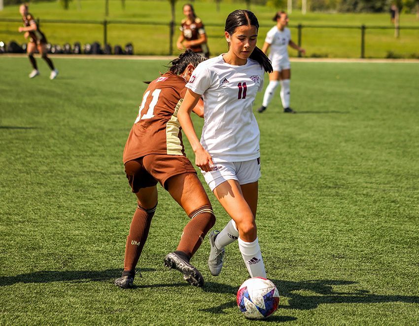 Two soccer players on a green field; one in a brown uniform defending against a player in white with the number 11.