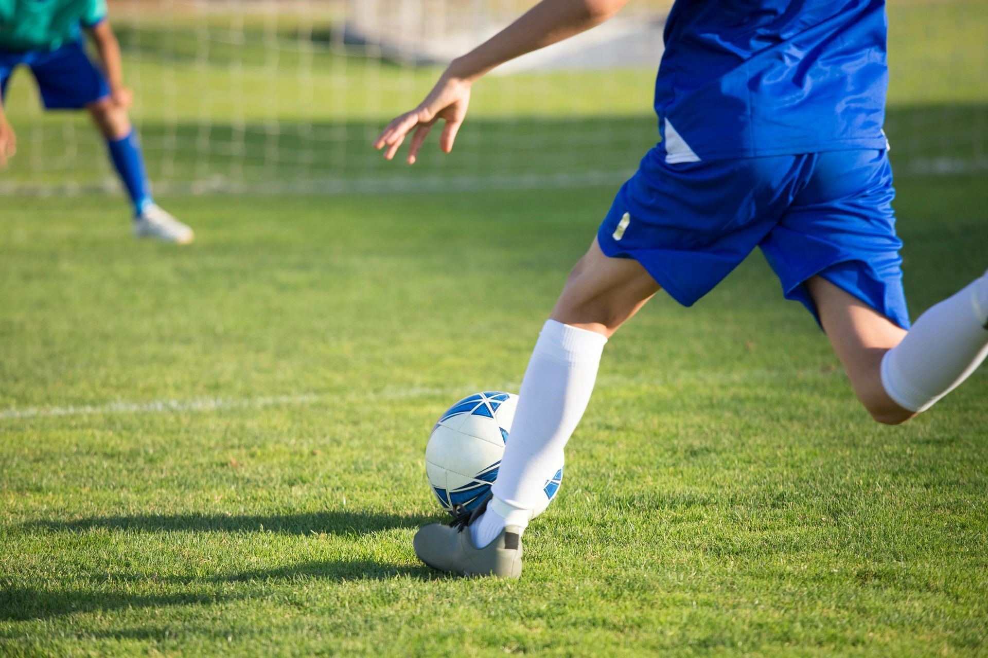 A player in a blue uniform kicks a soccer ball on a green field during a game.