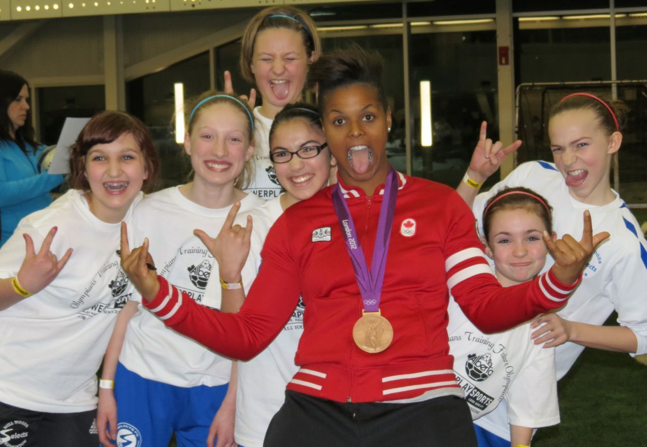 A group of people wearing matching white shirts and making hand gestures, with one wearing a red jacket and a medal.