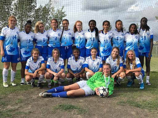 A soccer team in blue and white jerseys poses for a photo on a field, with a goalie sitting in front holding a soccer ball.