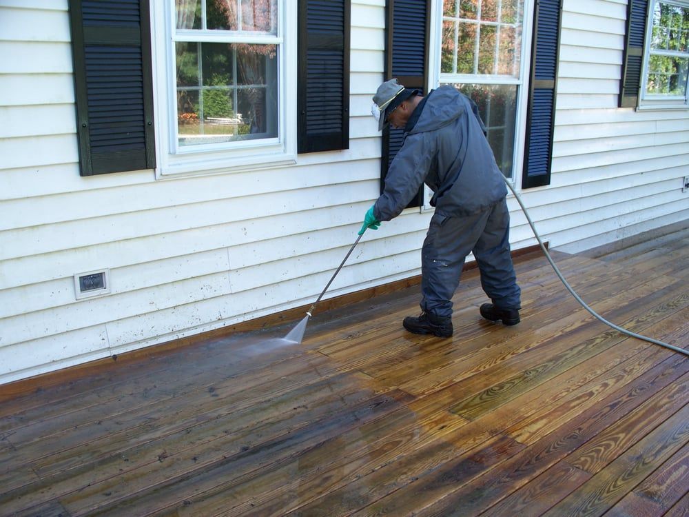 A man is cleaning a wooden deck with a pressure washer.