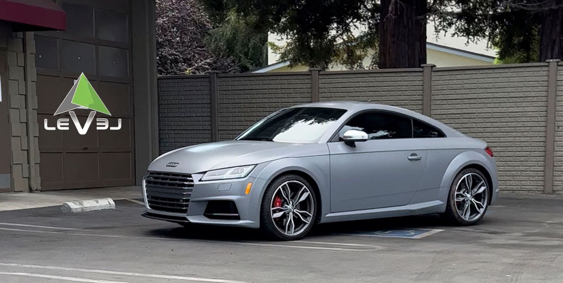 Silver sports coupe parked outdoors in front of a wall with a glowing logo sign