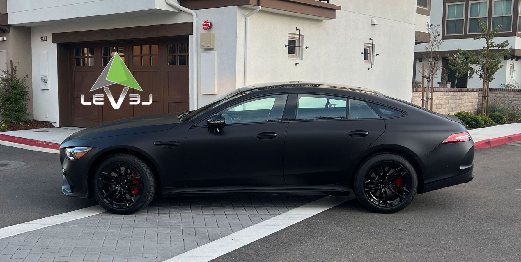 Black sedan parked outside a building with a LEVS sign on the wall.