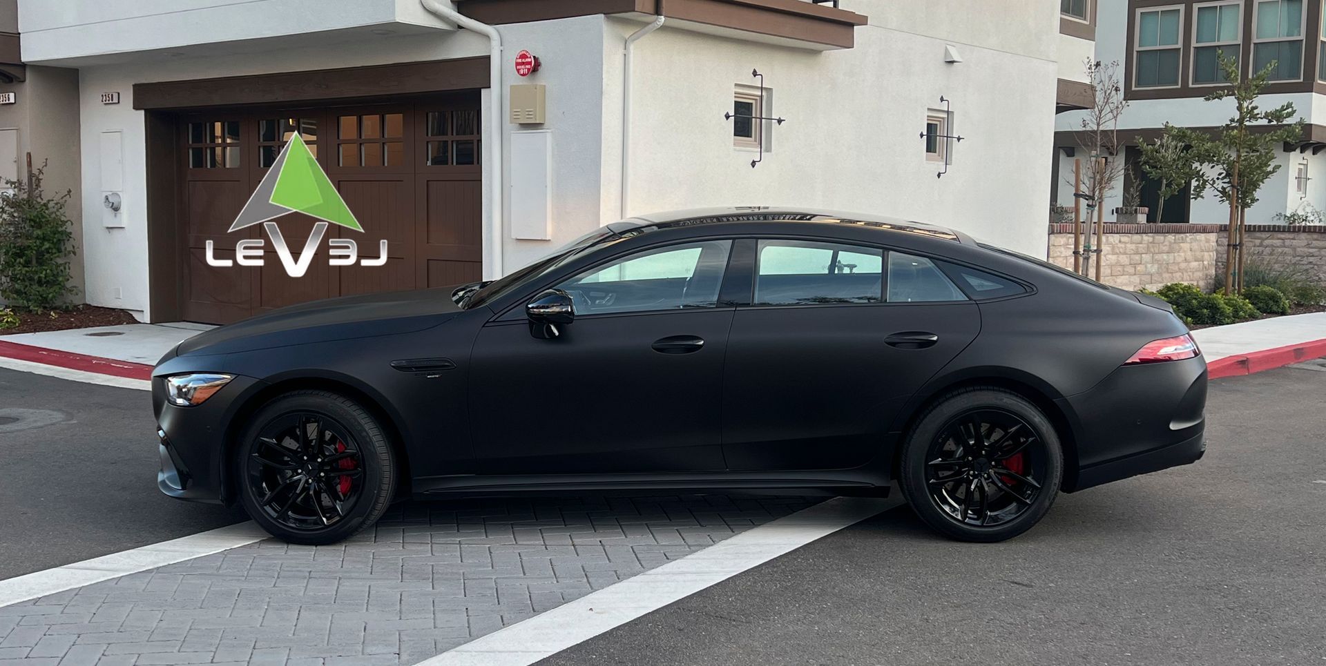 Black sedan parked outside a building with a LEVS sign on the wall.