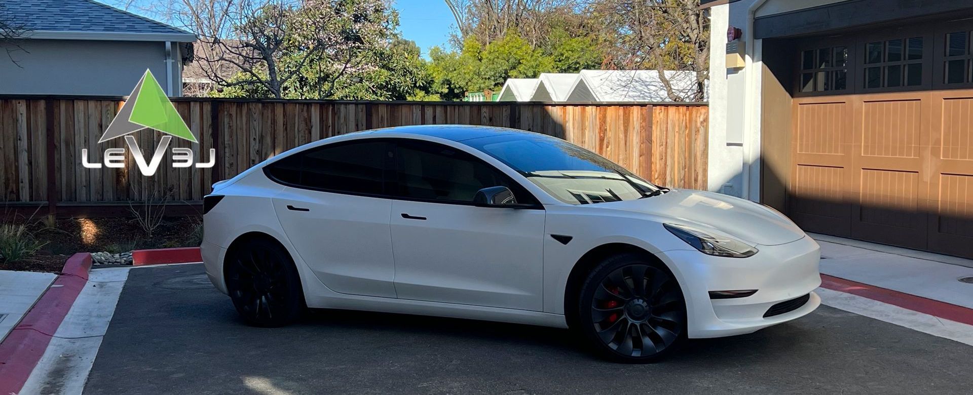 White sports sedan parked on a driveway beside a wooden fence in a sunny suburban yard.