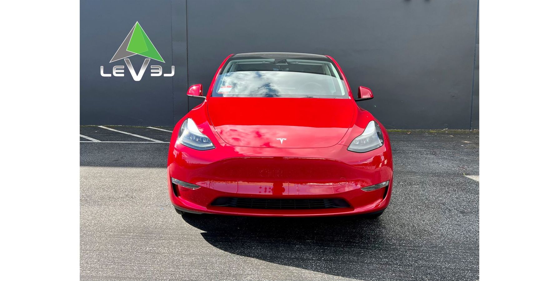 Front view of a red sports car parked on gravel in front of a dark wall with a logo.
