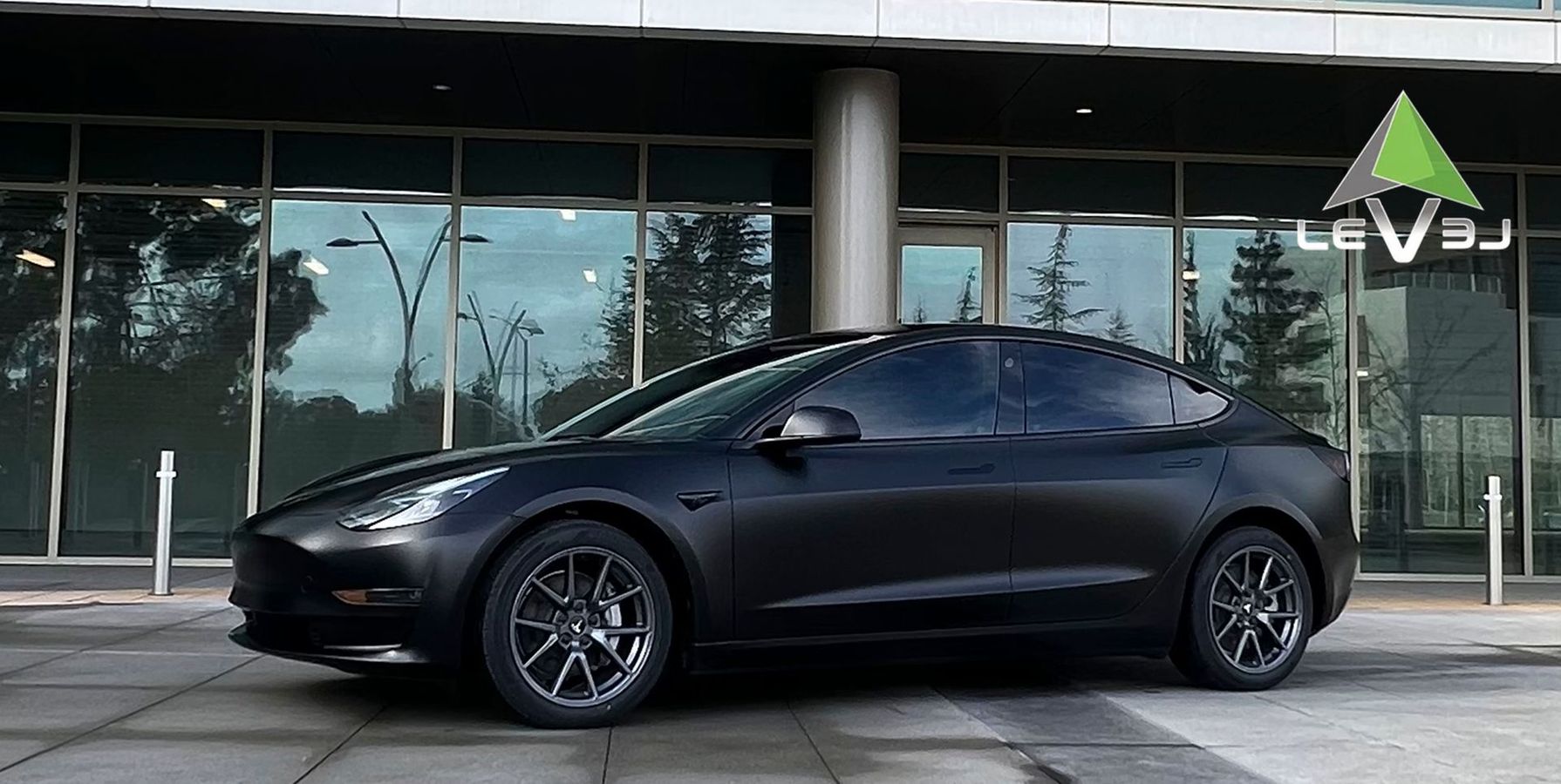 Black sedan parked in front of a glass building, side view in daylight.