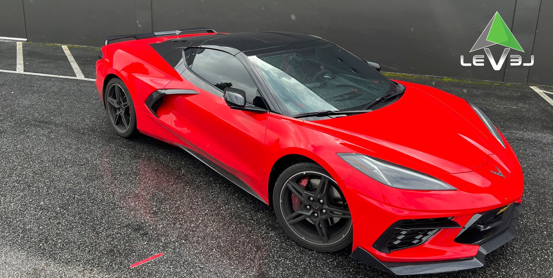 Red sports car parked on wet pavement in a parking lot, viewed from the front-left.