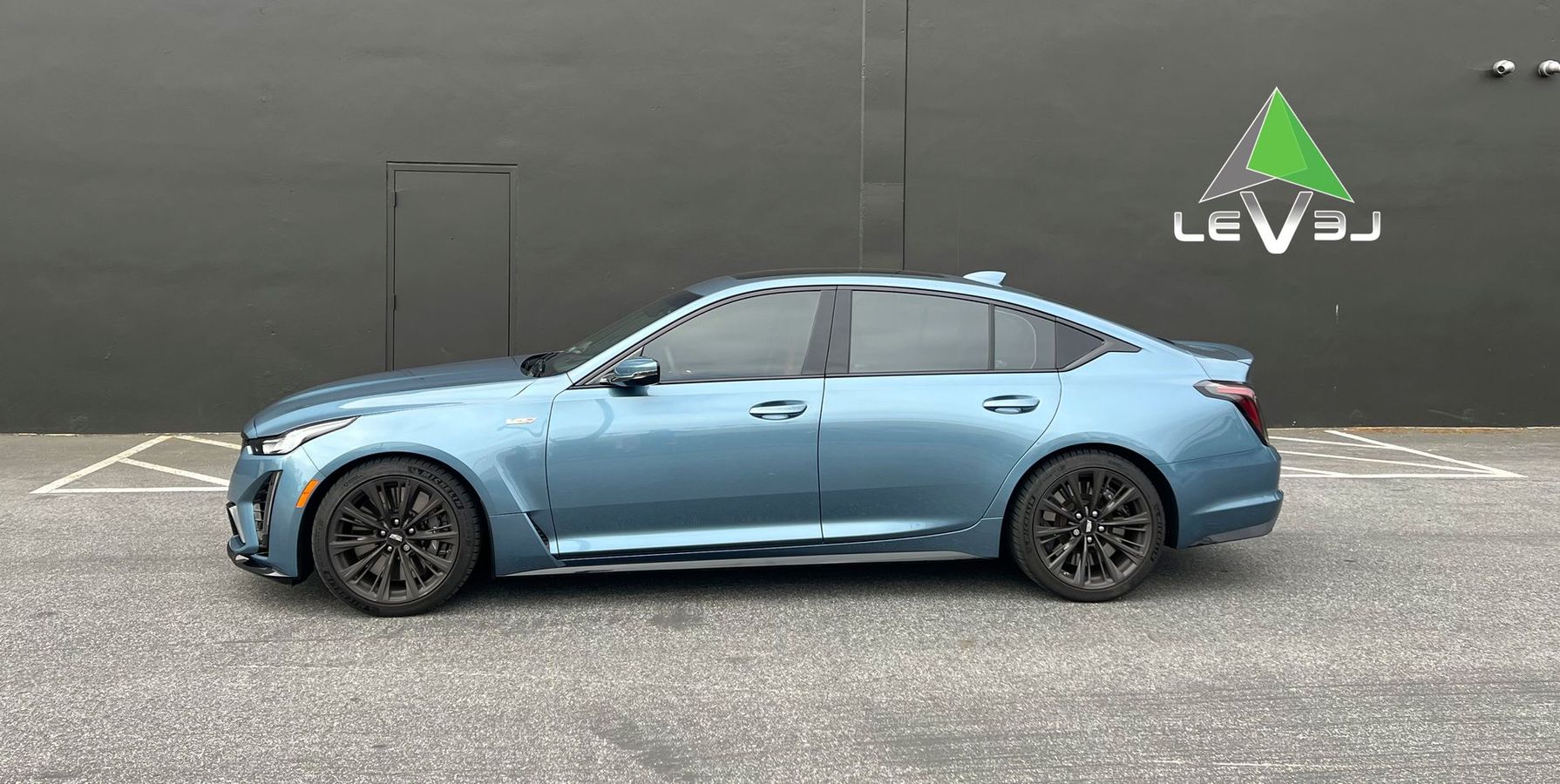 Light blue sedan parked in profile against a dark wall, with a LEVJ sign above.