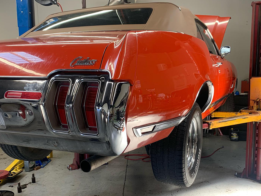 Red classic car on a lift in a garage, rear view with missing bumper and exposed exhaust