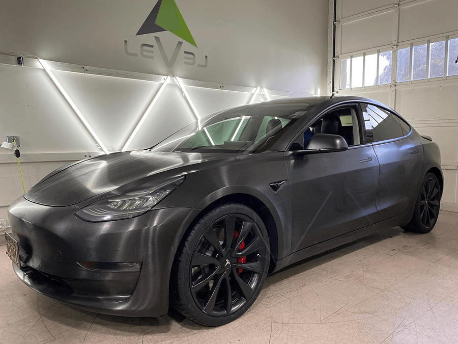 Matte black Tesla Model 3 in a showroom, angled front view with black wheels and red brake calipers