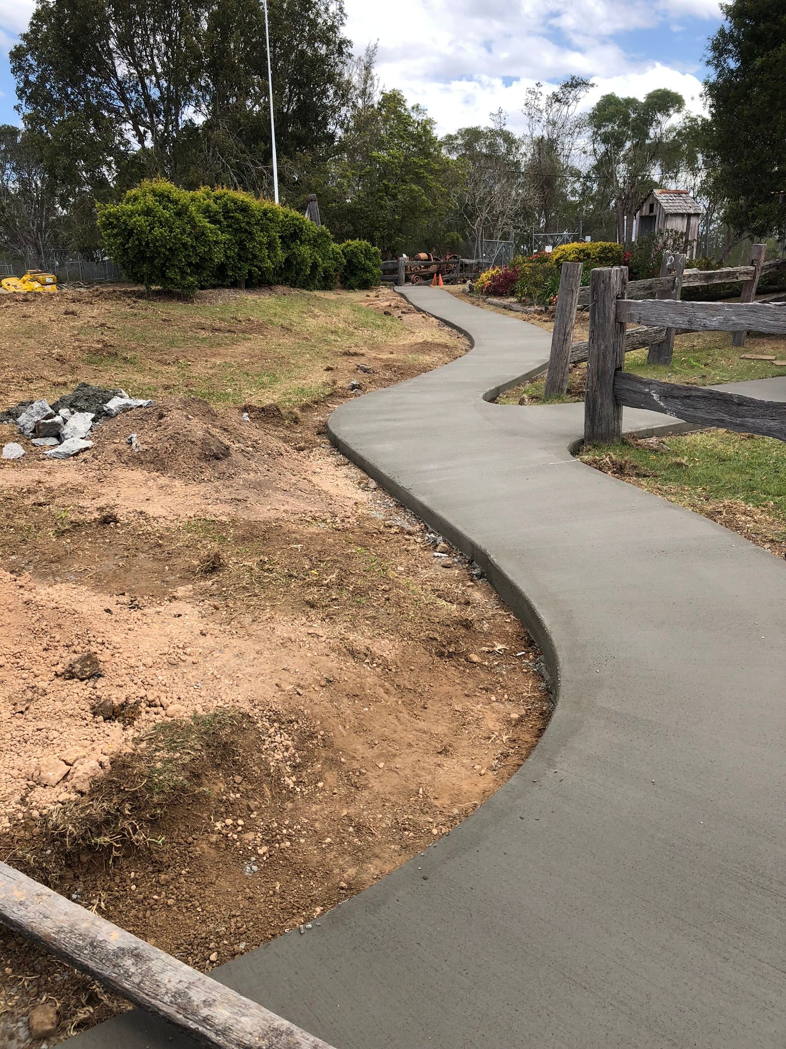 A Concrete Walkway is Being Built in a Park Next to a Wooden Fence — Grafton Concreting & Bobcat Services In South Grafton, NSW