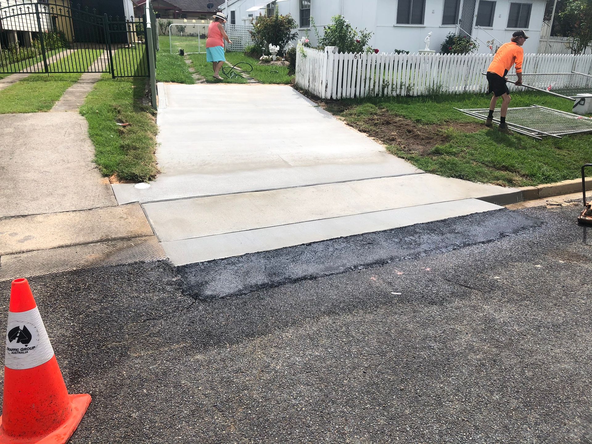 A Man is Painting a Driveway in Front of a House — Grafton Concreting & Bobcat Services In South Grafton, NSW