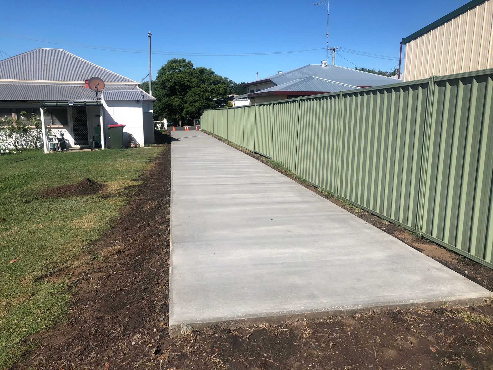 A Concrete Walkway Leading to a House With a Green Fence — Grafton Concreting & Bobcat Services In South Grafton, NSW
