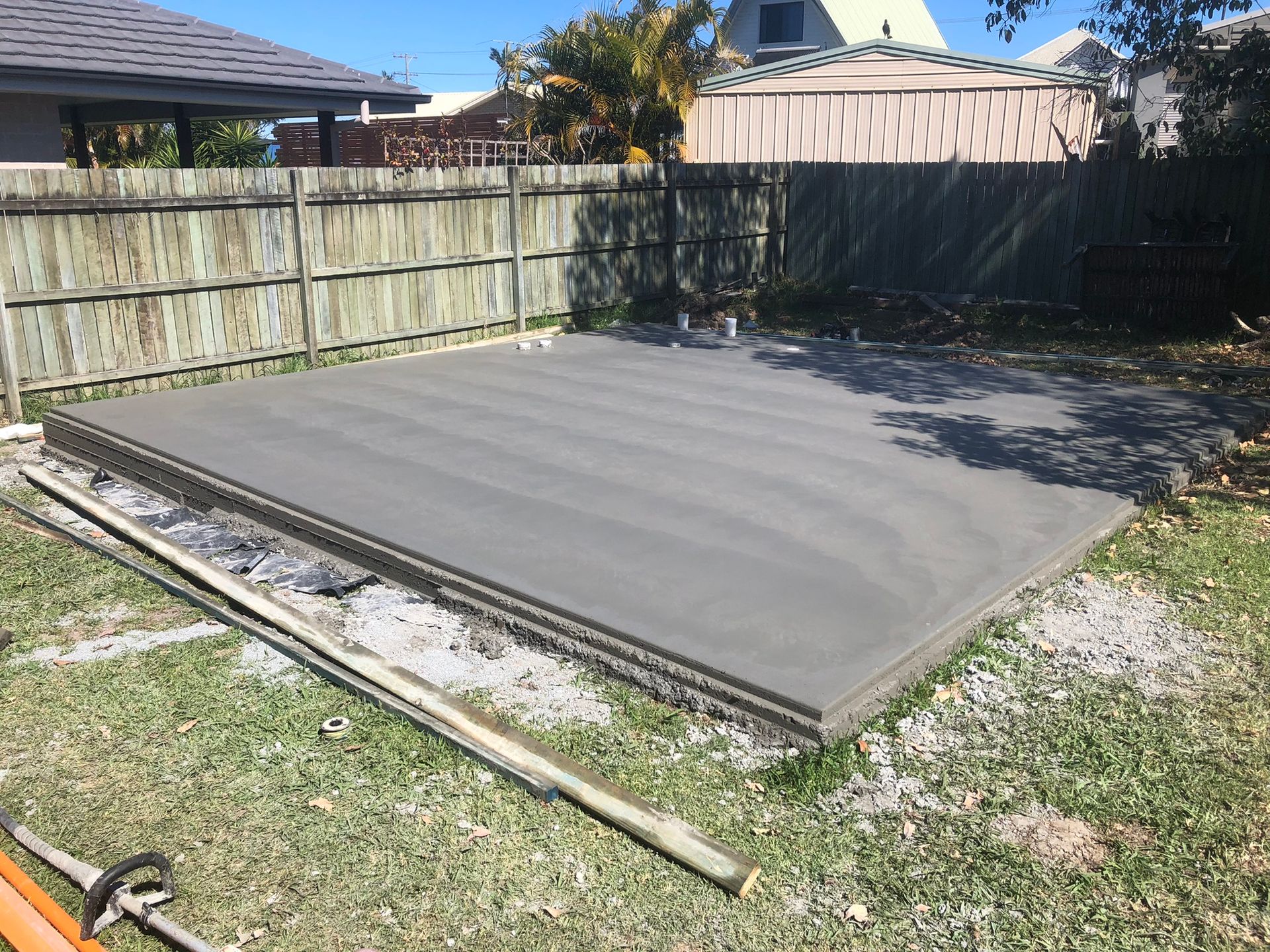 A Concrete Slab is Being Built in a Backyard Next to a Wooden Fence — Grafton Concreting & Bobcat Services In South Grafton, NSW