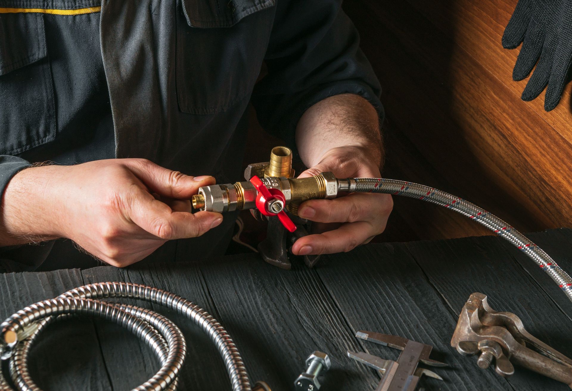 Hands connecting a gas hose to a brass valve with a red knob on a workbench with tools nearby