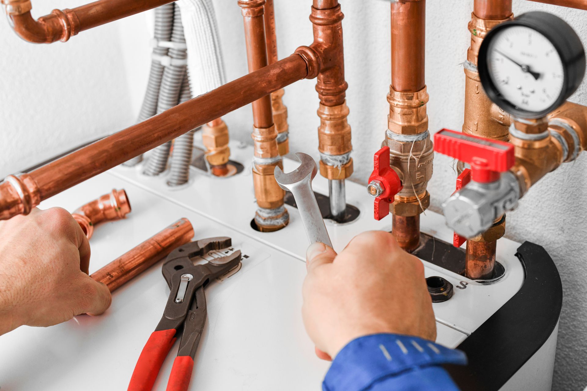 Technician tightening copper plumbing pipes with pliers beside a pressure gauge and red valve manifold