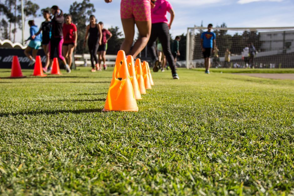 Orange training cones on a sports field with people jogging in the background
