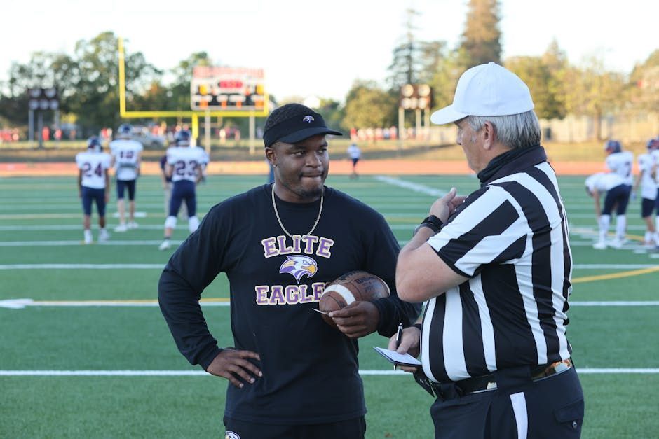 Football coach in black sweatshirt talking with a referee on a field during a game