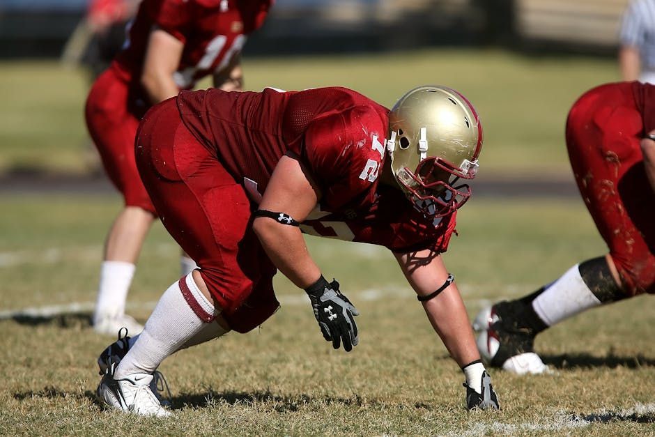 Football player in red uniform crouches at the line of scrimmage on a field