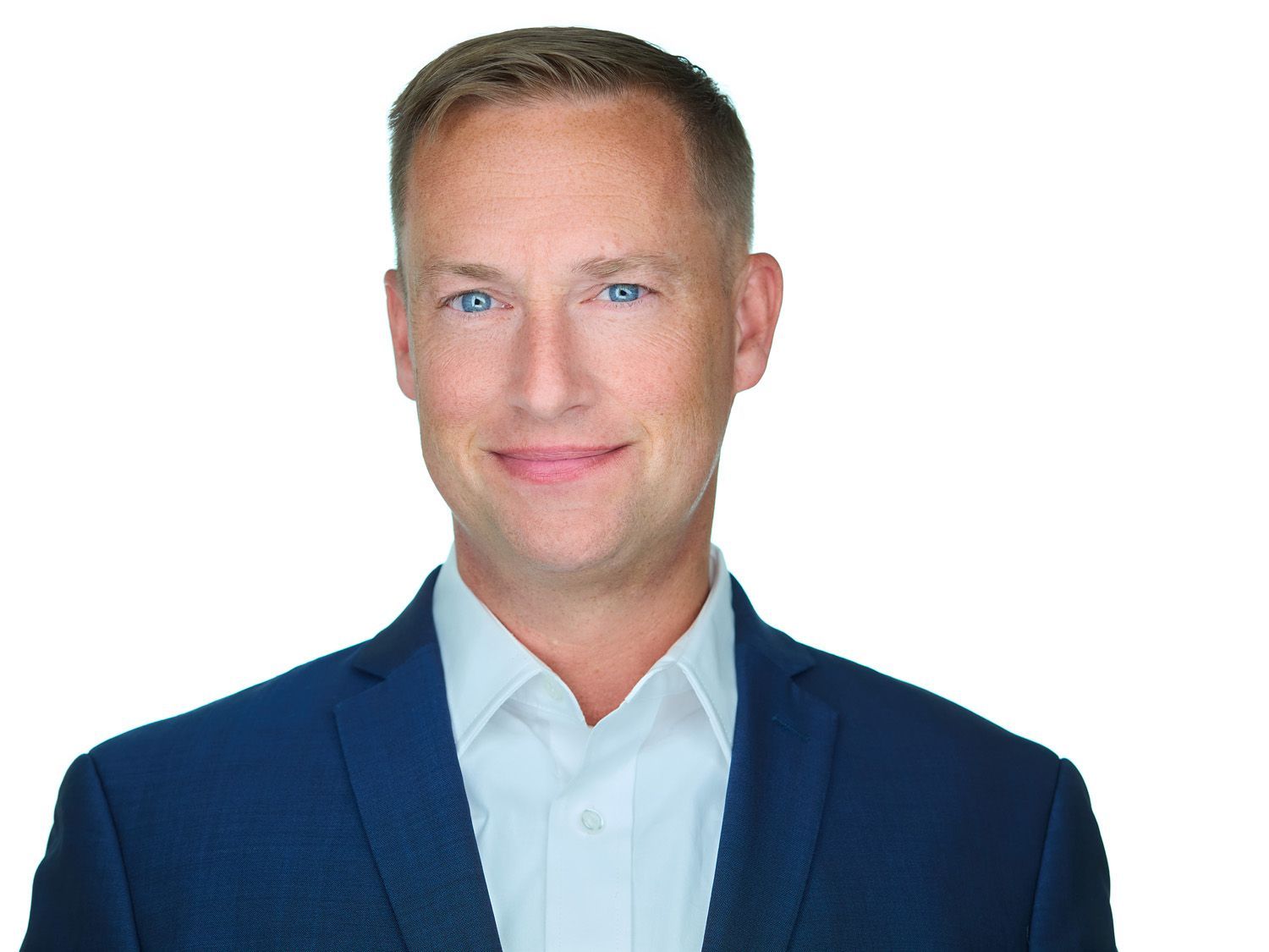 Man in a blue blazer and white shirt smiles, looking at the camera against a white background.