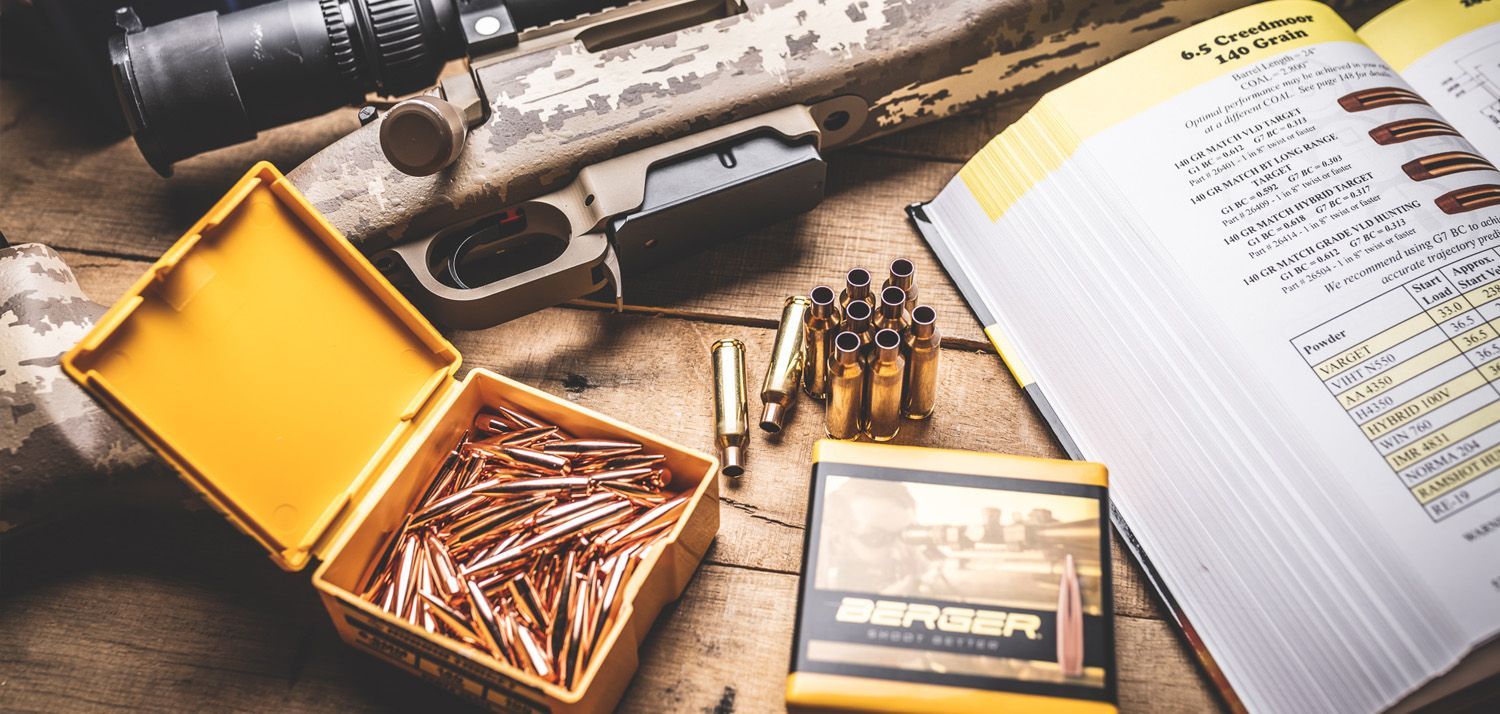 Puška, naboji  Berger Bullets, odprta škatla nabojev in priročnik za polnjenje na leseni površini.