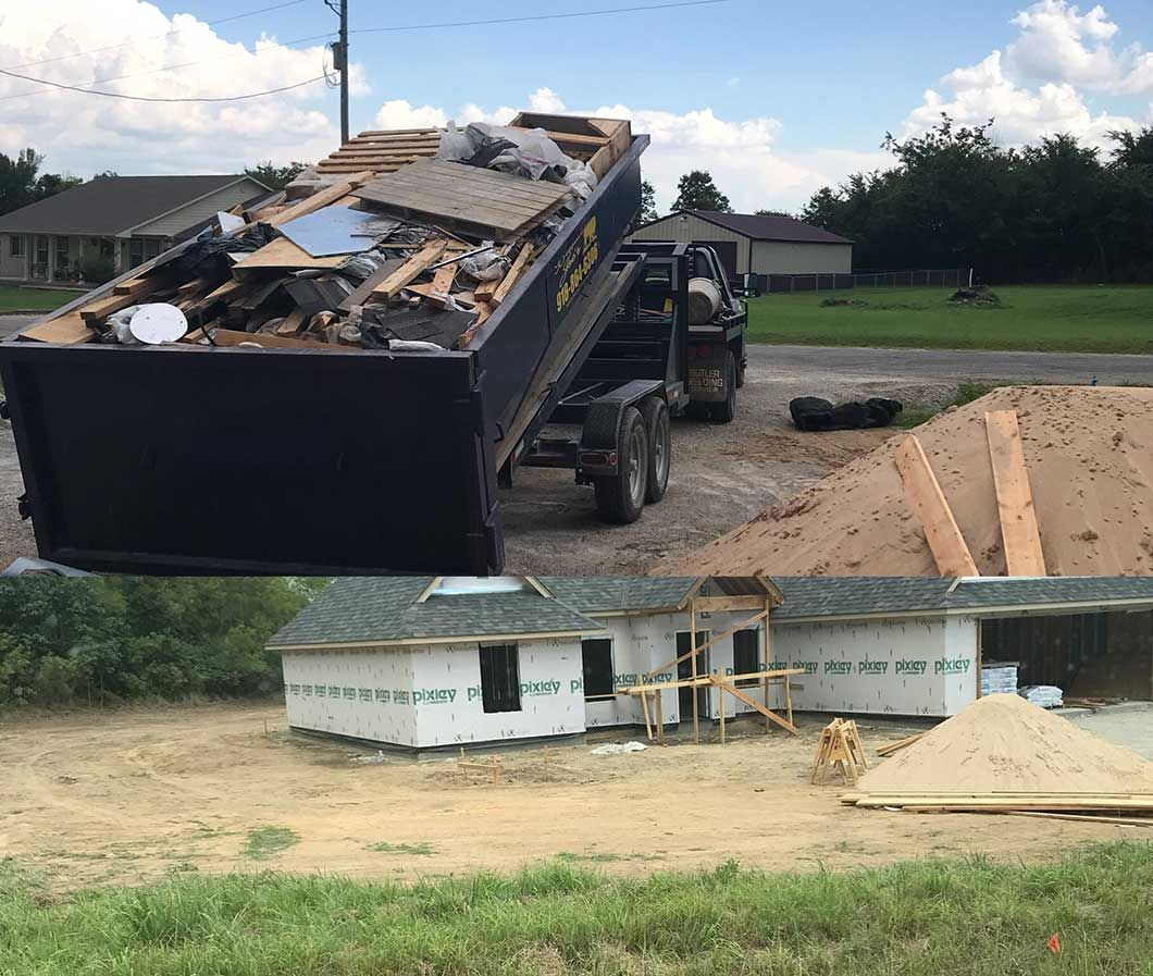 Dump truck unloading demolition debris beside a small house under construction, with a pile of sand nearby.