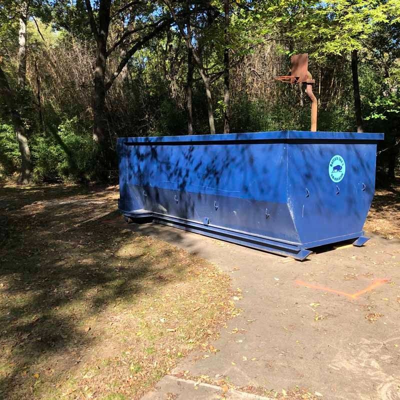 Blue dumpster on a wooded path with a tree stump rising from its top