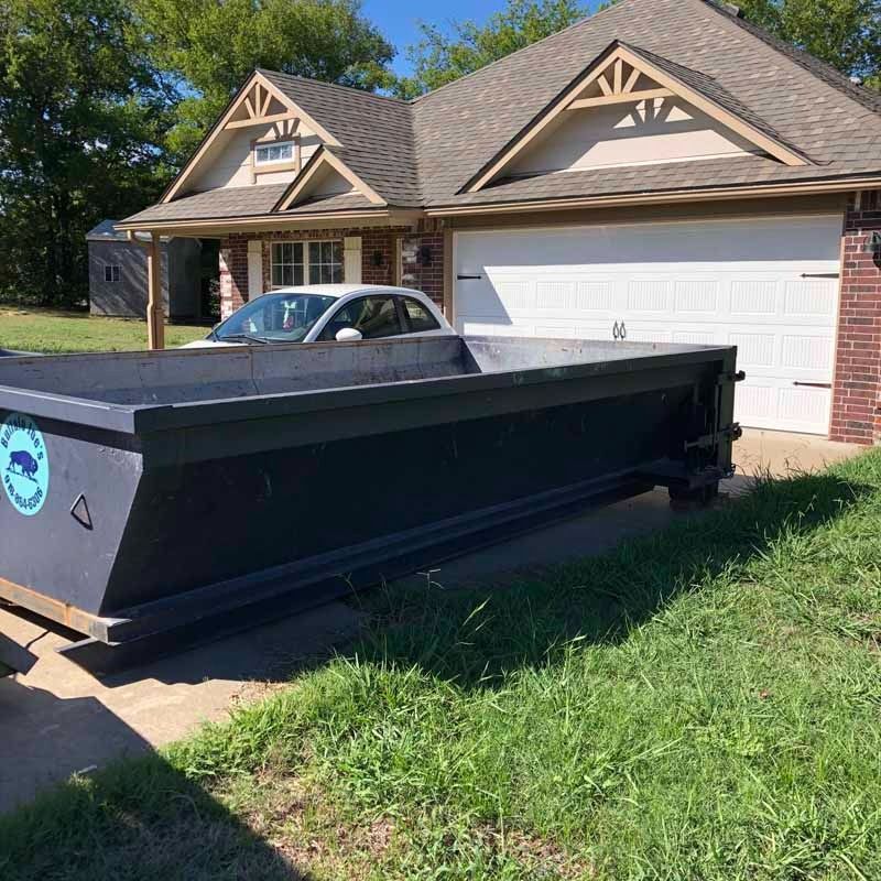 Black dumpster trailer parked in front of a suburban house with a white garage door
