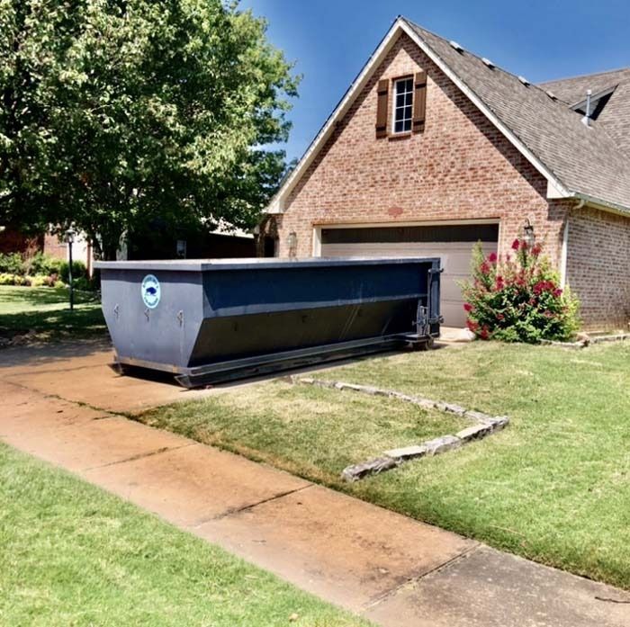Large black dumpster on a driveway in front of a brick house with a garage
