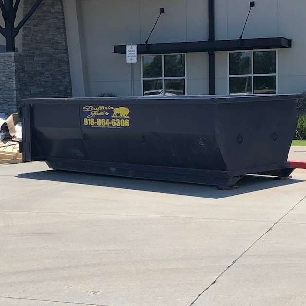 Black dumpster outside a building on a concrete lot, with yellow lettering on the side.