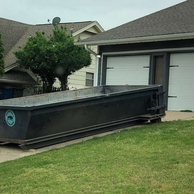Large black dumpster parked on a driveway beside a suburban garage and lawn