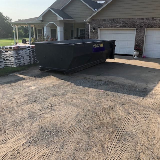 Black dumpster on a driveway in front of a suburban house and garage