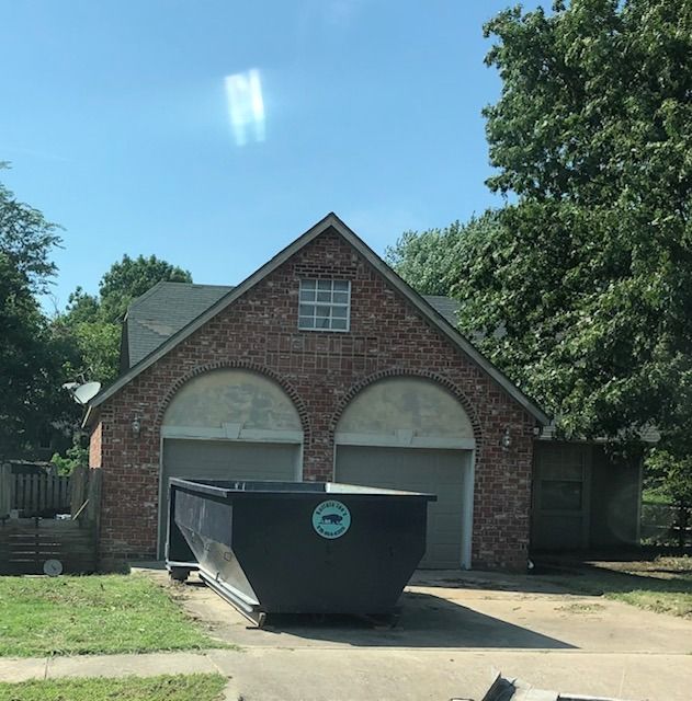 Brick garage with two white doors and a black dumpster in the driveway under a blue sky