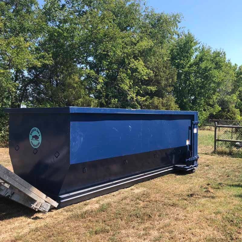 Large blue and black dumpster or storage container on grass near trees and a fence