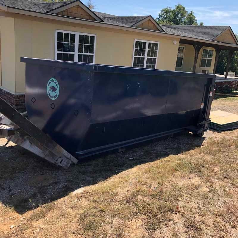 Large dark blue dumpster on a driveway in front of a beige house