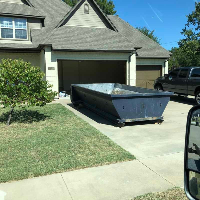 Large blue dumpster on a driveway in front of a suburban garage.