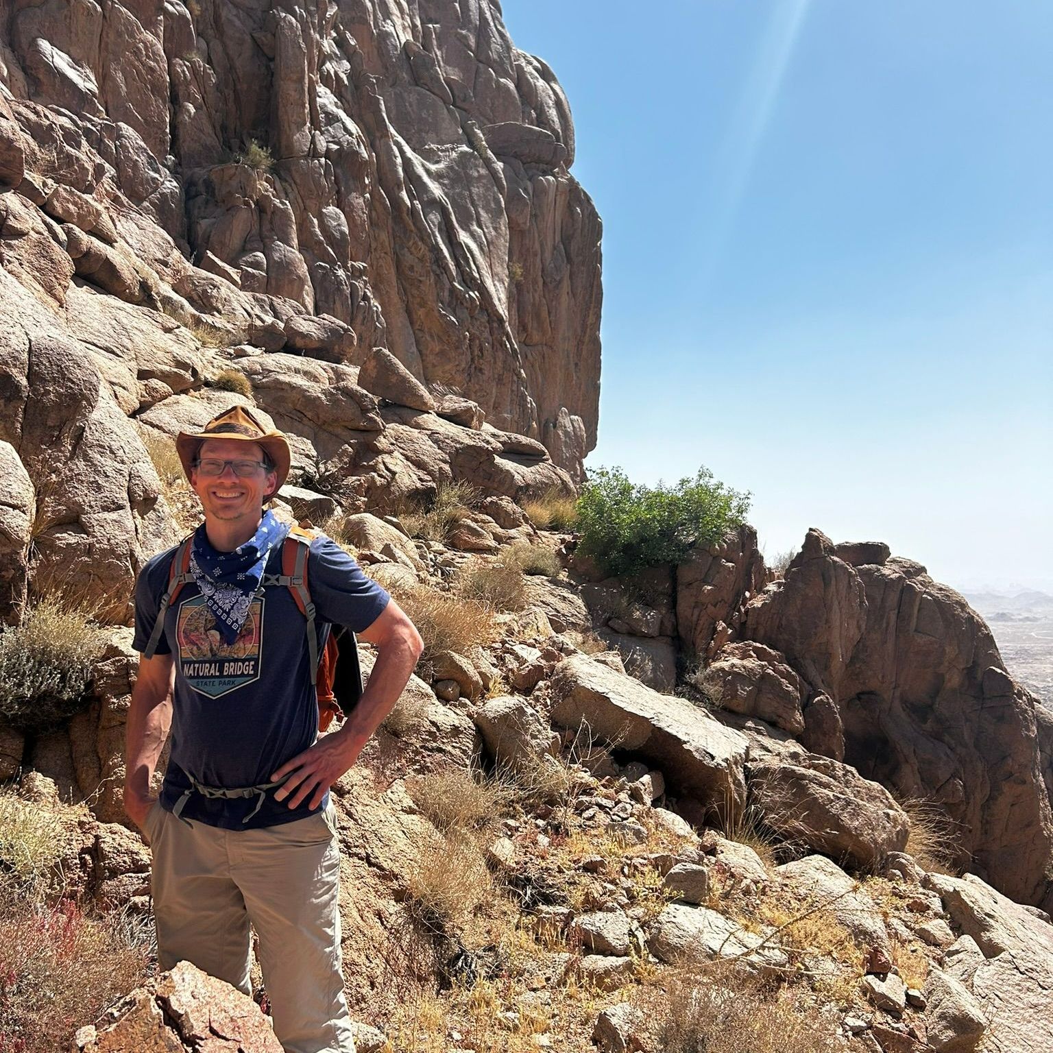 A man wearing a hat and sunglasses is hiking the Real Mount Sinai
