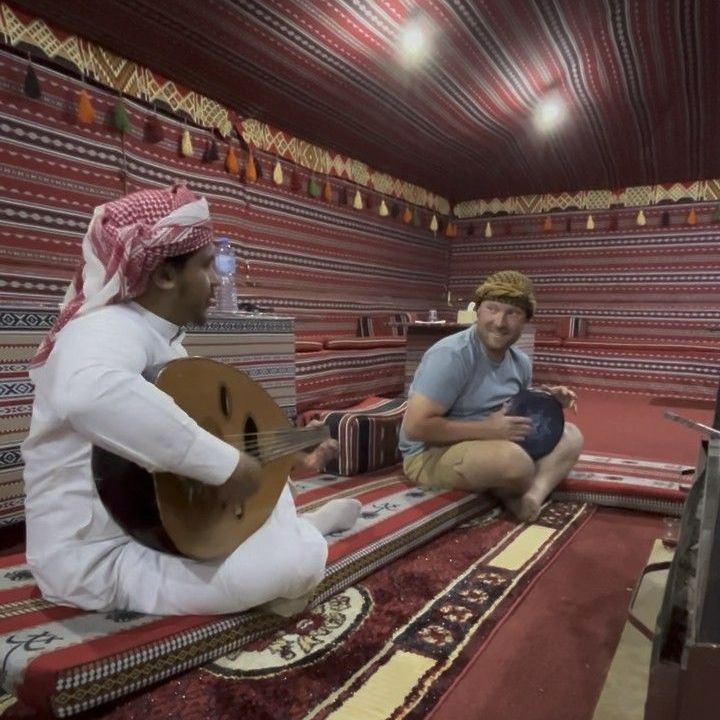 A bedouin is playing a guitar while another man plays a drum