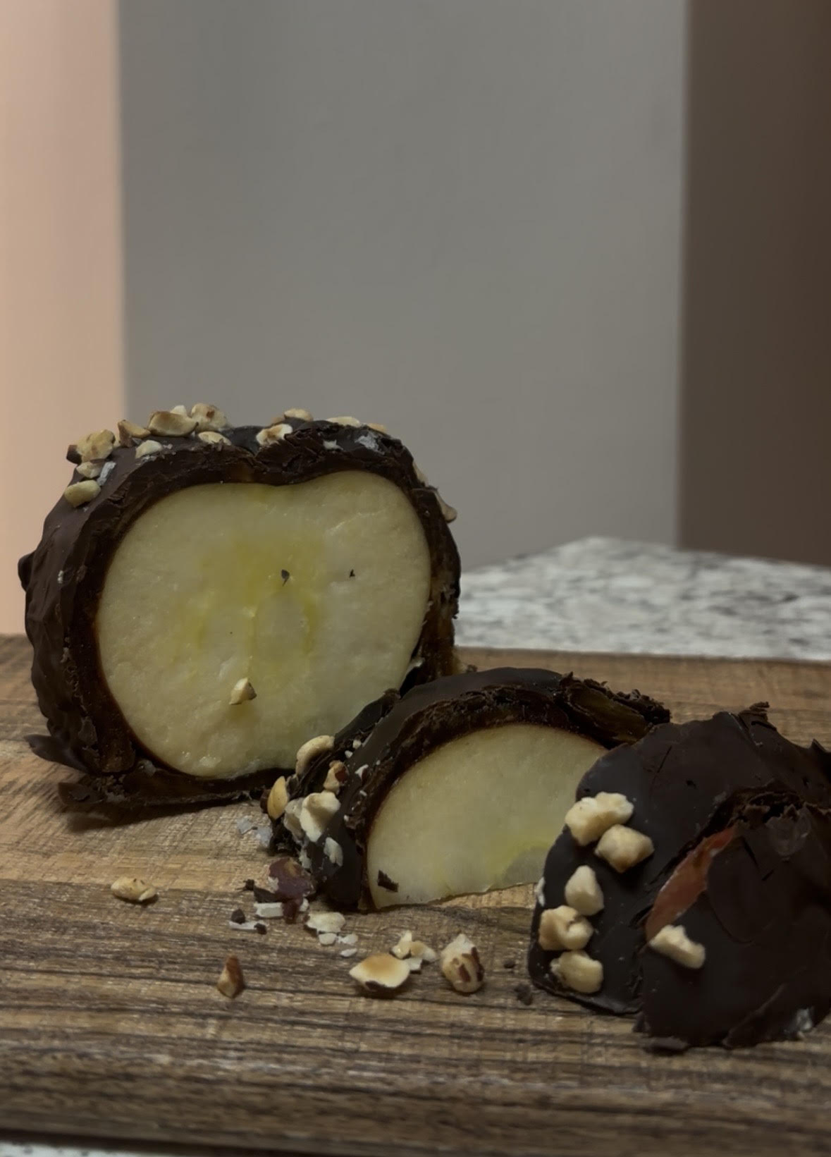 Sliced date caramel apple coated in dark chocolate and chopped nuts, served on a wooden board