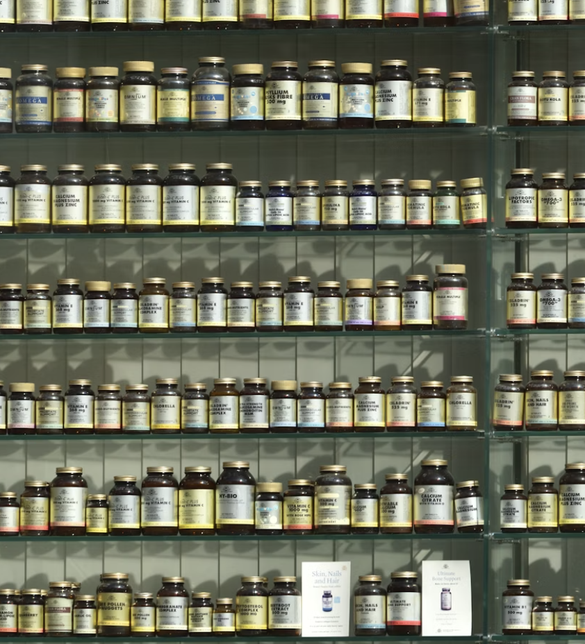 Multiple glass shelves tightly packed with dozens of uniform dark glass bottles of dietary supplements, vitamins, and minerals, showcasing a wide variety of nutritional products.