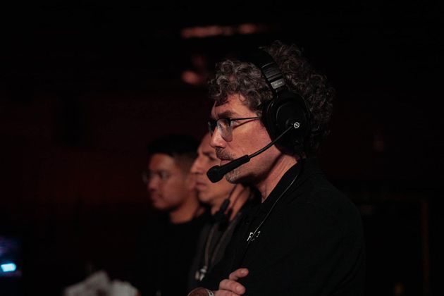 A man wearing headphones and a microphone is standing in a dark room.