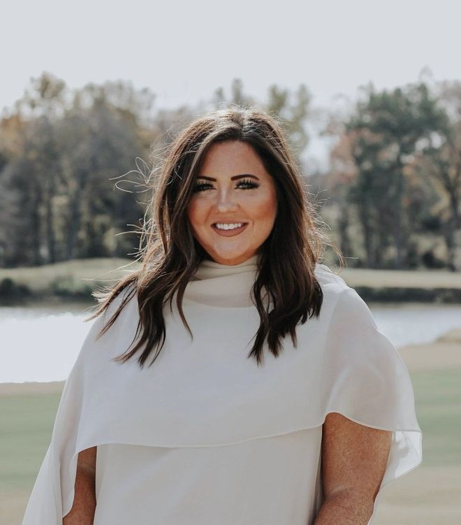 A woman in a white dress is standing in front of a body of water.